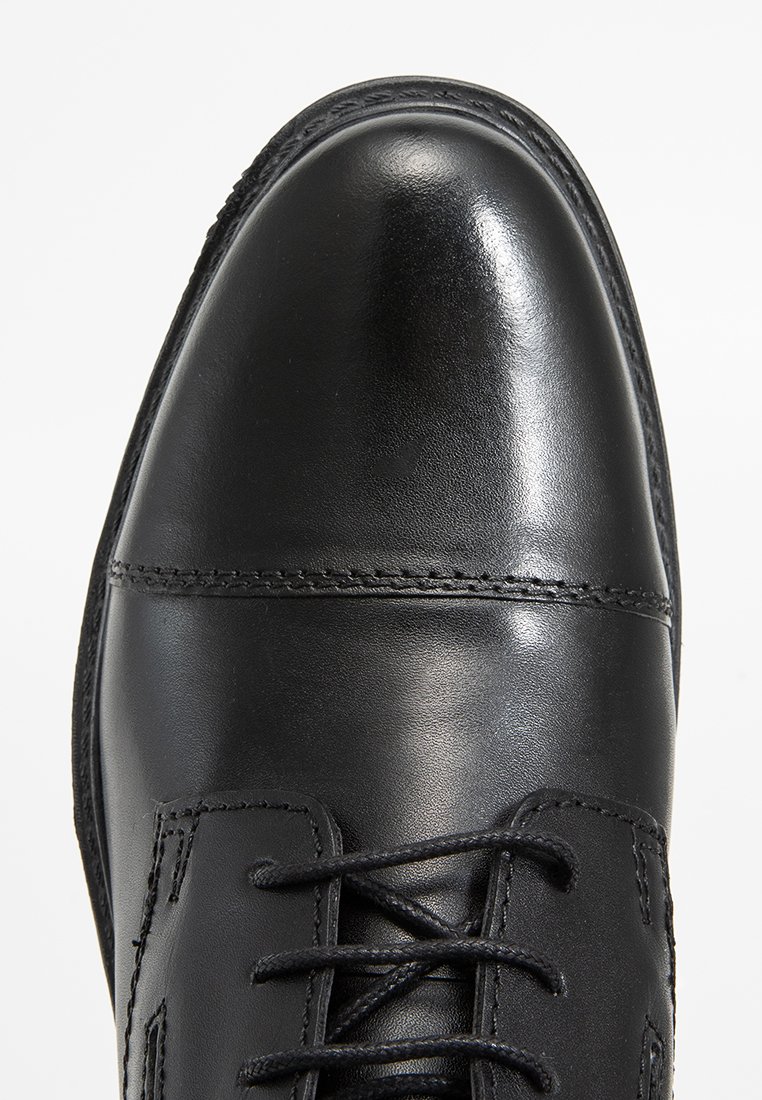 Chaussure habillée en cuir noir avec une surface lisse et polie, un système de laçage fermé, et des détails de couture subtils, dotée d'un bout arrondi.