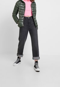 Polstret grøn jakke, pink cropped top og mørkegrå rullede jeans, parret med sorte høj-top sneakers med hvide såler og snørebånd.