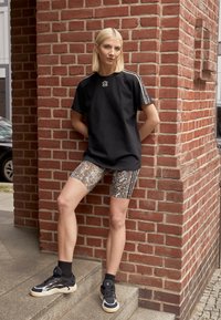 Svart överdimensionerad t-shirt med broderad logga, matchad med cykelbyxor i ormtryck med sidostråk. Svarta sneakers med cremefärgade sulor.