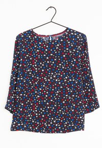 Blouse aux motifs d'étoiles bleues, rouges et blanches sur fond noir ; elle comporte des manches longues et un col rond avec un petit détail en forme de goutte.