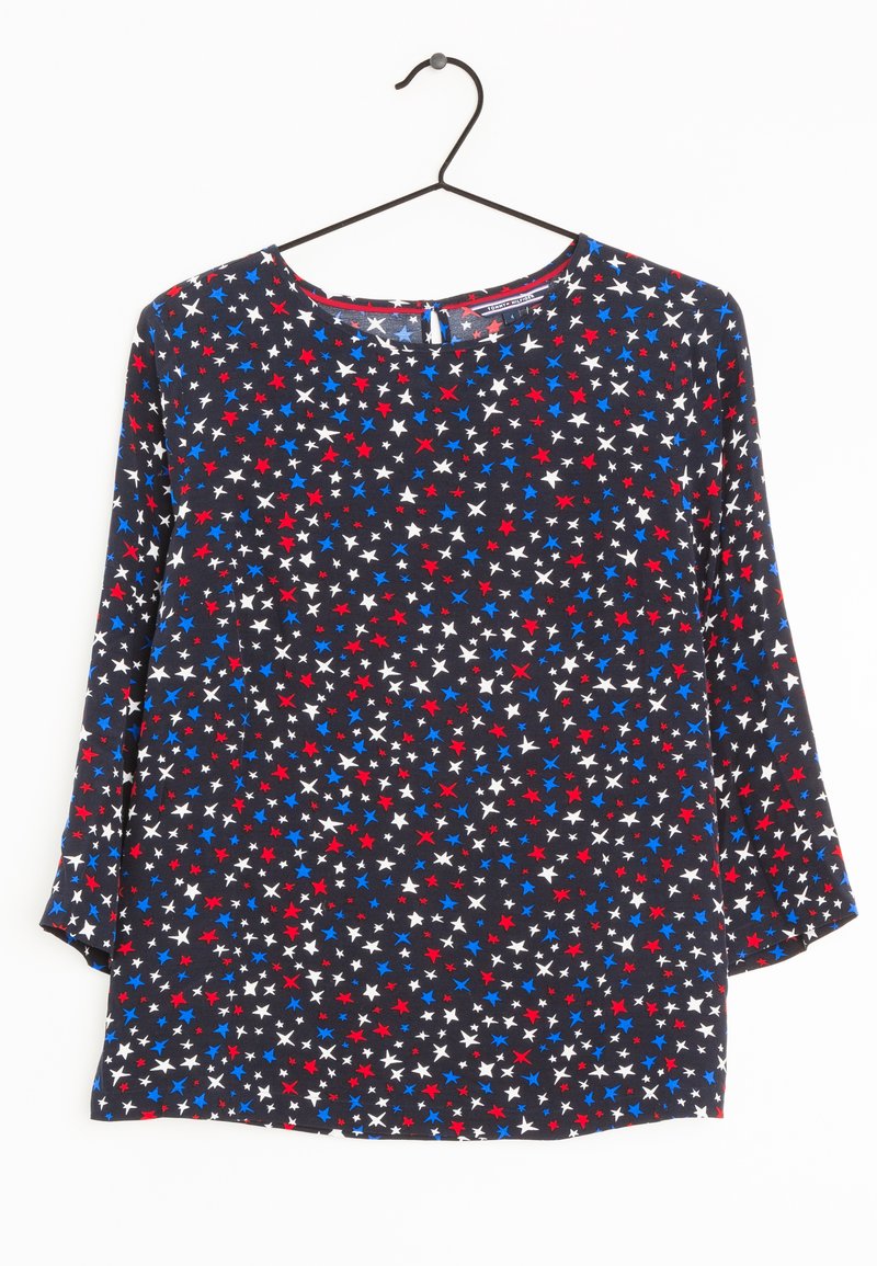 Blouse aux motifs d'étoiles bleues, rouges et blanches sur fond noir ; elle comporte des manches longues et un col rond avec un petit détail en forme de goutte.