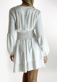 Witte jurk met lange mouwen, voorzien van een gesmokte taille, gelaagde rok en een zachte, soepele stof met een losse pasvorm en zachte val.