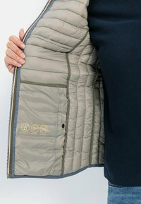 Leichte, wasserabweisende, winddichte Jacke mit einem ge quilteten beigen Innenfutter, grauen Akzenten und gedruckten Pflegeicons innen. Mit Reißverschluss.