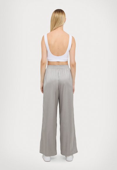 Witte mouwloze top gecombineerd met lichtgrijze wijde satijnen broek; de top heeft een lage rug en de broek heeft een elastische tailleband.