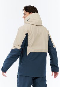 Waterdichte jas in beige en marineblauw, met een capuchon, ritszakken en verstelbare manchetten, met een slank, modern ontwerp.
