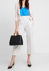 Ljusrosa jacka med öppen front över en blå volangtopp, kombinerad med vita, randiga korta byxor och svarta spetsiga klackskor. Svart handväska med sköldpaddsmönstrade handtag.