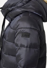 Gros plan sur une veste d'hiver noire matelassée avec capuche relevée et écusson logo CMP sur le haut du bras.