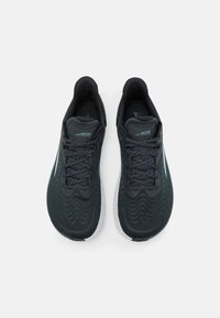 Scarpe sportive nere con una tomaia texturizzata, dotate di lacci scuri e una suola bianca. Presentano un sottile motivo a onde stampato di lato.