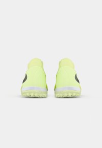 Un par de zapatillas deportivas de color amarillo neón con suelas blancas, vistas desde la parte trasera sobre un fondo blanco liso.