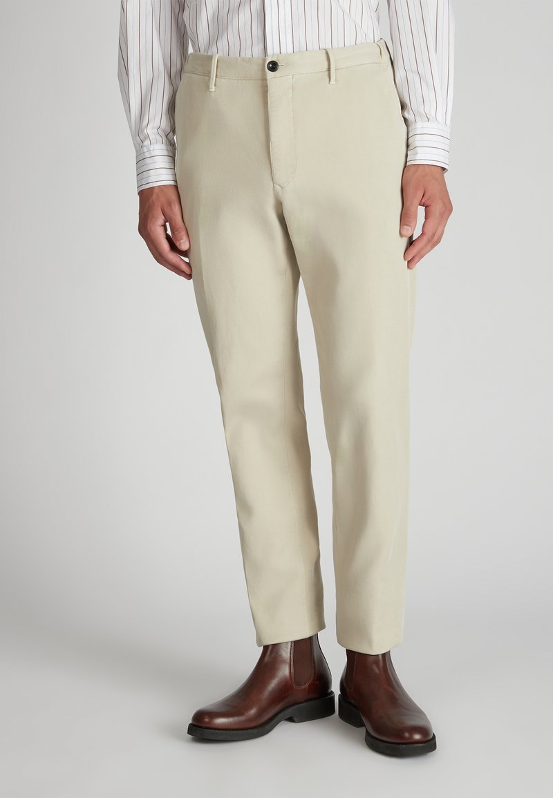 Jasnobeżowe spodnie o dopasowanym kroju, z zamkiem błyskawicznym, zapięciem na guzik i kieszeniami po bokach, zestawione z brązowymi skórzanymi botkami typu chelsea.