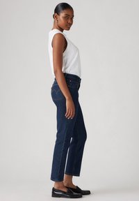 Tumed sinine denim kõrge vöökohaga teksapüksid otse lõikega, õrn fade ja eriline tagatasku disain. Kombineeritud valge ilma varrukateta topiga.