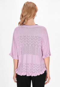 Top lavorato a maglia di un morbido colore viola chiaro con un motivo testurizzato, dotato di maniche corte e orlo a volant. Sezioni trasparenti creano un effetto a strati.