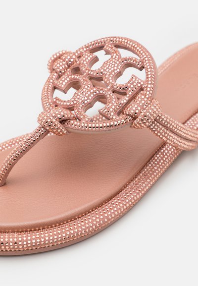 Sandal flip-flop warna rose gold dengan desain potongan lingkaran dan tali yang bermotif tekstur dihiasi dengan manik-manik kecil yang berkilau. Alas kaki yang lembut dan halus.