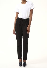Zwarte, aansluitende broeken met een strik taille, gemaakt van zachte stof. Gekenmerkt met een eenvoudig wit t-shirt en spitse zwarte schoenen.