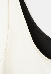Gros plan de décolletés superposés de vêtements sans manches blancs et noirs montrant la texture du tissu et les détails des coutures.
