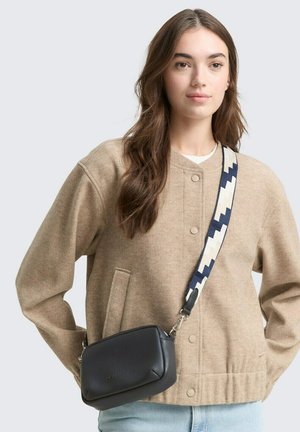 Tan fleece jacket met een ronde kraag en drukknoopjes, gecombineerd met een kleine zwarte leren schoudertas en een gemusterde strap.