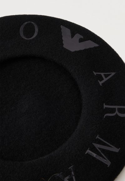 Chapeau en feutre noir avec des lettres embossées et un symbole d'aigle autour du bord sur fond blanc.