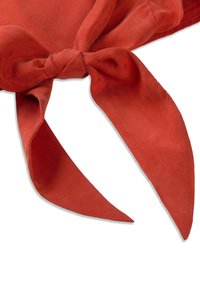 Écharpe en tissu doux rouge nouée de manière lâche avec deux extrémités effilées sur un fond blanc.