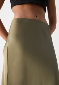 Jupe en satin vert olive avec une texture lisse et un design ajusté, dotée d'une taille haute et de lignes épurées.