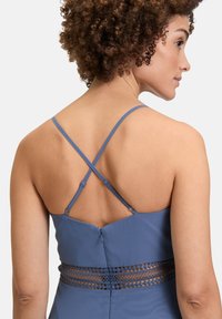 Robe bleue avec un design de bretelles croisées à l'arrière. Présente une accents en dentelle texturée à la taille et une fermeture éclair.