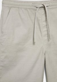 Shorts décontractés beige clair avec taille élastique et cordon de serrage noué, dotés de poches latérales et de coutures apparentes.