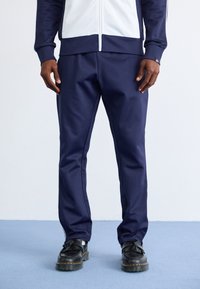 Marineblauwe sportbroek met een gladde textuur, met een slim fit en subtiele stikdetails. Gepaard met zwarte schoenen.