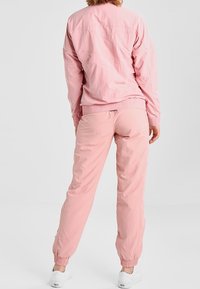Pink lightweight jacket and matching jogger pants, featuring elastic cuffs and a simple design. Smooth texture with a casual fit.