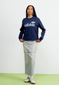 Marinblå långärmad skjorta med vita ränder och "adidas"-logotyp, kombinerad med en ljus denimkjol. Neutrala sneakers kompletterar outfiten.