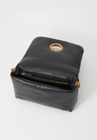 Bolsa de couro preta com forma retangular plana, apresentando um acabamento em metal dourado e um compartimento com fecho de correr. Superfície texturizada e detalhe circular.