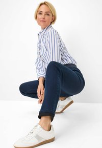 Jeans in denim blu abbinati a una camicia a righe bianca e blu e a sneaker bianche. I jeans hanno un design aderente e orli arrotolati.