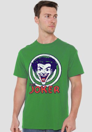 Mann trägt grünes T-Shirt mit großem Joker-Gesicht Grafik und rotem Text mit der Aufschrift "The Joker" vorne, blickt nach links.
