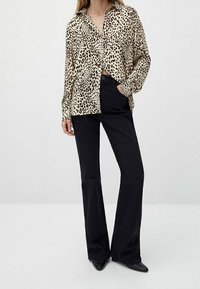 Leopardprint knapup skjorte lavet af glat stof, båret med høj talje sorte flare bukser. Skjorten har krave og en løs pasform.