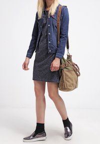 Jeansjacka, grå klänning med ett subtilt mönster, metalliska slipskor och en tan axelväska med gröna accenter och handtag.