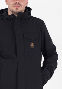 Zwarte jack met een ritssluiting aan de voorkant, kap en drukknoopzak. Voorzien van een logo-opdruk, gestructureerde stof en elastische manchetten voor een goede pasvorm.