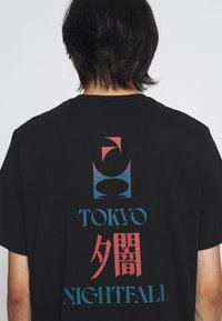T-shirt en coton noir avec un design graphique au dos, comprenant le texte stylisé "TOKYO" et "NIGHTFALL" en bleu et rouge, accompagné de formes géométriques.