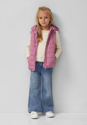 Lila puffer vest met een capuchon, gestikt ontwerp, gecombineerd met een crèmekleurige geribbelde longsleeve top en lichtblauwe spijkerbroek met uitlopende pijpen. Witte sneakers.