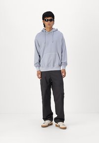 Lysblå hætte trøje med forlommer, kombineret med grå cargobukser og hvide sneakers, og sorte solbriller.