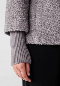 Maglione grigio testurizzato con polsini a coste. Il tessuto appare morbido e peloso, mentre il polsino aggiunge un contrasto nella texture e una vestibilità aderente.
