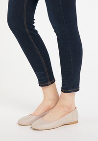 Beżowe skórzane baleriny z okrągłym noskiem i niskim obcasem, w zestawie z ciemnoniebieskimi skinny jeansami z pomarańczowym przeszyciem w pobliżu dołu.