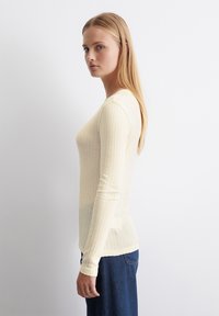 Ljusgul långärmad ribbad topp gjord av ett mjukt, texturerat tyg. Har en figursydd silhuett och rund halsringning. Matchas med blåjeans.
