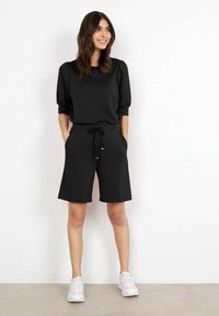 Černý dvoudílný outfit, který obsahuje top s krátkým rukávem a kulatým výstřihem a šortky s elastickým pasem a bočními kapsami.