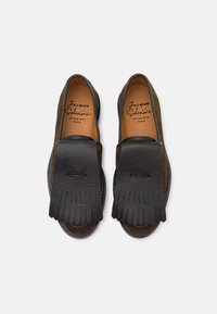 Mocasines de cuero negro con un diseño de flecos texturizados, forro marrón suave y acentos de talón de ante marrón en contraste.