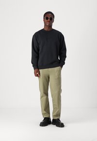 Svart sweatshirt med präglad logotyp, ljusgröna cargobyxor och svarta chunky skor. Solglasögon fulländar den avslappnade outfiten.