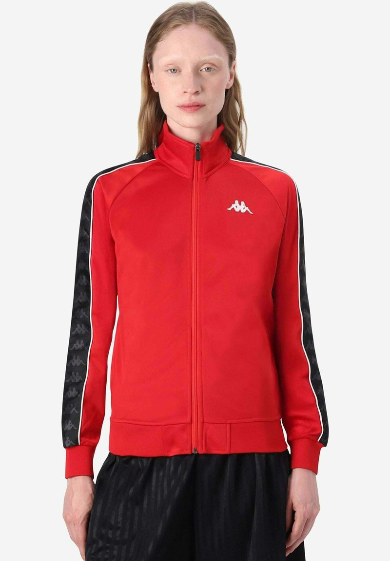 Giacca tuta rossa con zip, con dettagli a strisce nere e bianche e logo Kappa sul petto; tessuto morbido con design aderente.