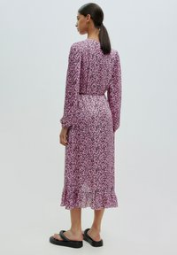 Rosa Kleid mit schwarzem Blumenmuster, langen Ärmeln und einem Rüschensaum. Aus leichtem Stoff gefertigt, tailliert und mit schwingender Silhouette.