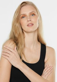 Schwarzes Tanktop mit rundem Ausschnitt, weichem Stoff und dünnen Trägern. Leicht gewelltes Haar und natürliches Make-up. Hautton ist hell.