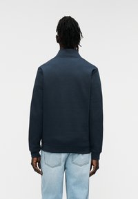 Μπλε ναυτικό φούτερ με ψηλό γιακά, λεία υφή, εφαρμοστά μανίκια και τελείωμα, συνδυασμένο με τζιν παντελόνι σε ανοιχτό μπλε χρώμα.