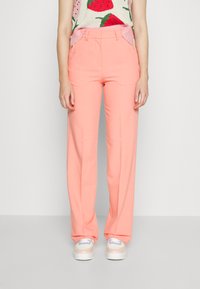 Calças largas de tom rosa claro com dois bolsos frontais e passadores para cinto. Combinadas com uma blusa texturizada com um padrão de morangos.