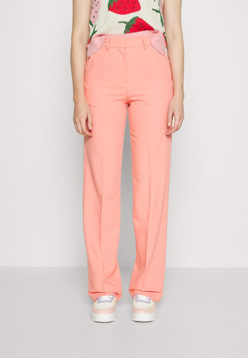 Calças largas de tom rosa claro com dois bolsos frontais e passadores para cinto. Combinadas com uma blusa texturizada com um padrão de morangos.