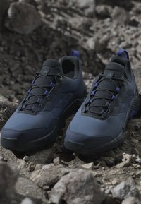 Mörkblå atletiska skor med en texturerad yta, svarta detaljer och snörning. Skorna har en vadderad krage och en gedigen sula för bra grepp.